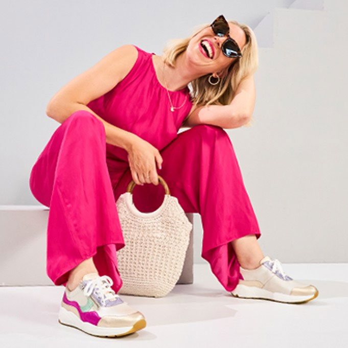 FRau in rotem Jumpsuit mit Sneakern von Solidus und einer Tasche sitz auf einer Stufe